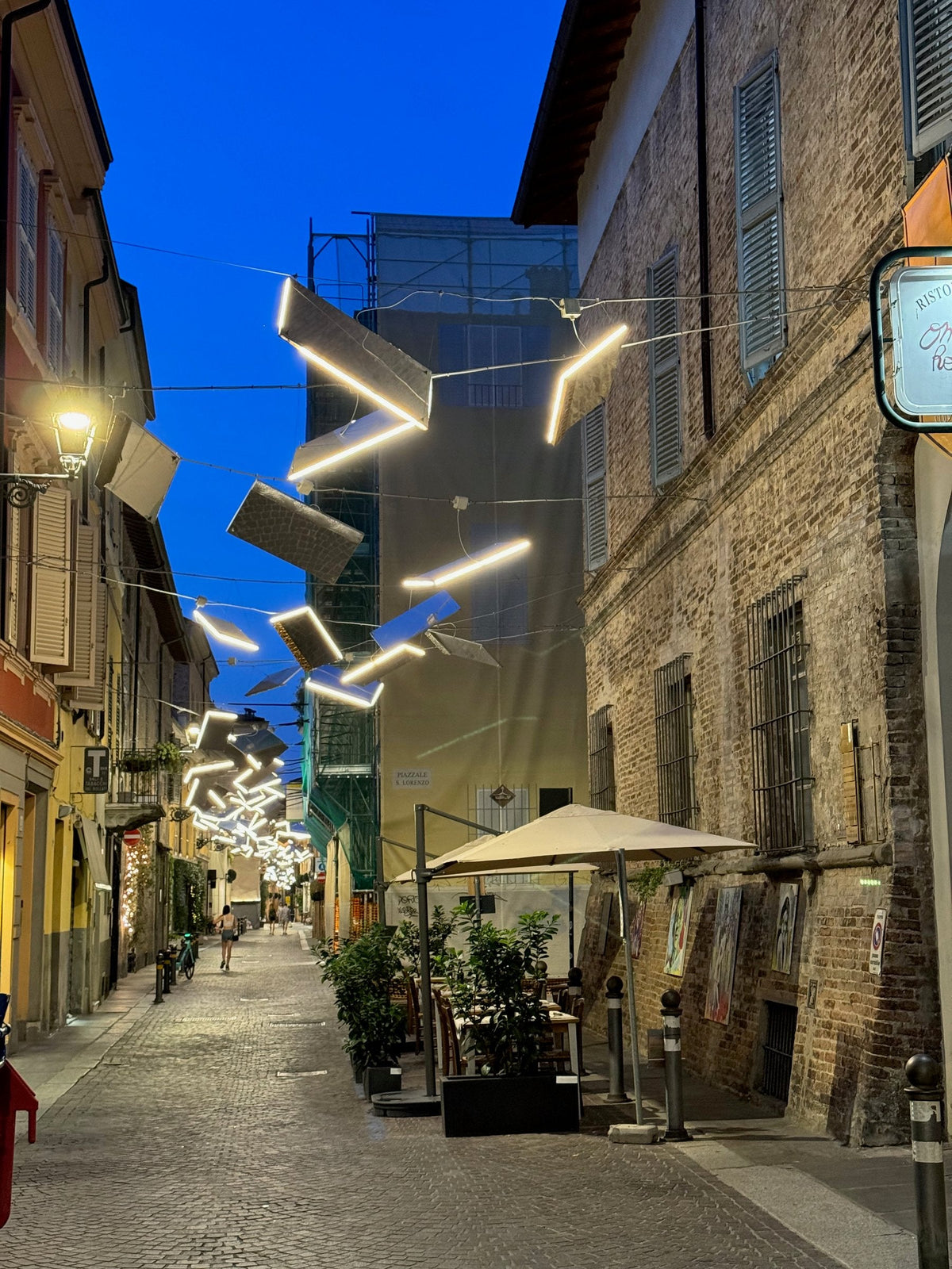 A lane in Parma's old town at dusk under a modern light installation