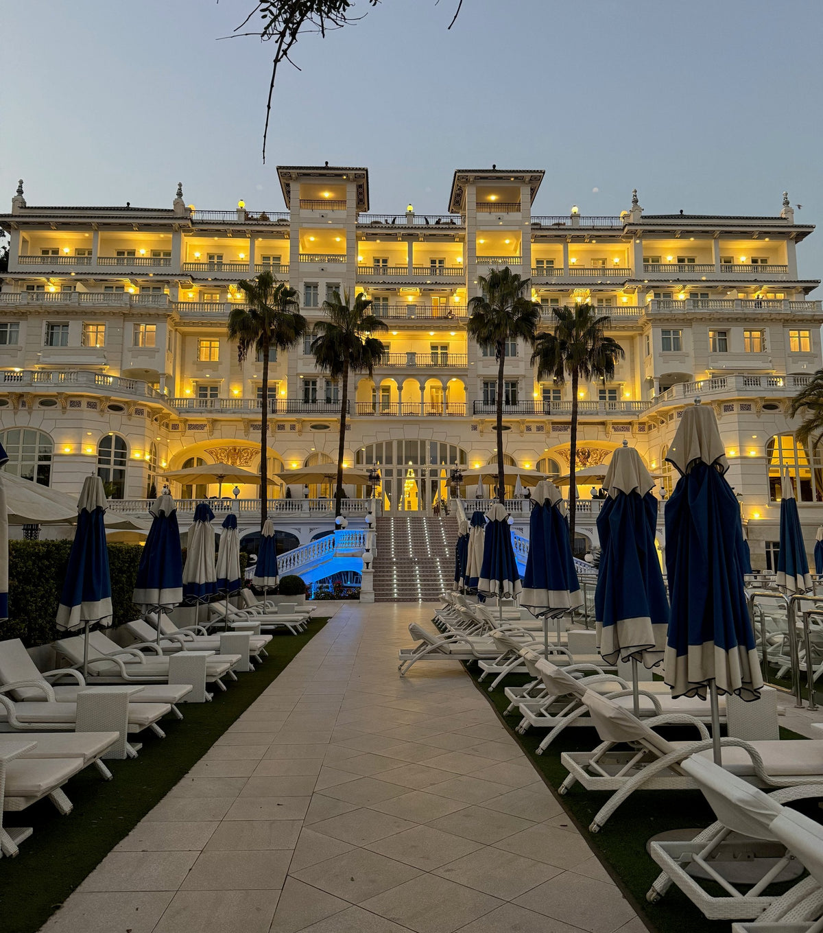 The Gran Hotel Miramar lit up at dusk, seen from the pool garden with its palms and parasols